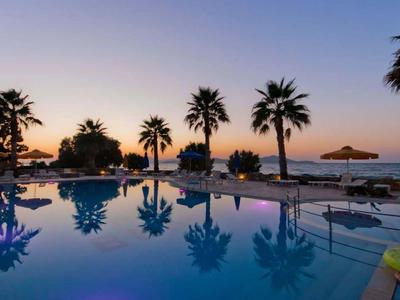 Abendlicher Hotelpool mit Palmen, Sonnenliegen und ruhiger Meereskulisse im Hintergrund.