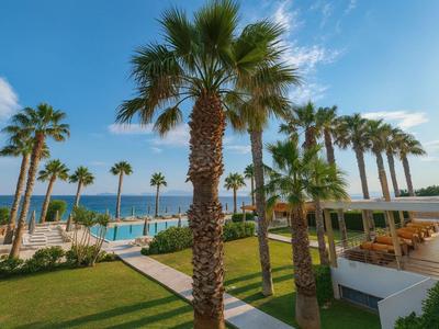 Hotel mit Palmen, Pool und Meerblick bei sonnigem Wetter.
