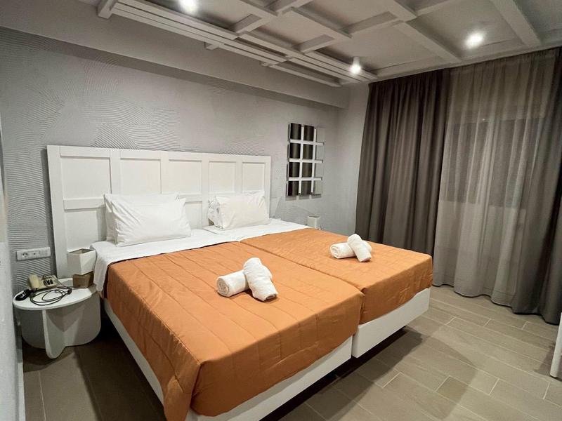 Moderní hotelový pokoj se dvěma jednolůžky, oranžovým povlečením a šedými závěsy.