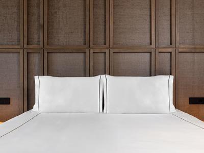 Modern hotel bed with white bedding against a wooden paneled wall