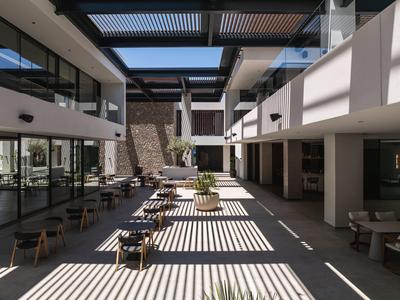 Modern hotel courtyard with chairs, tables, and sunlight through a lattice roof.