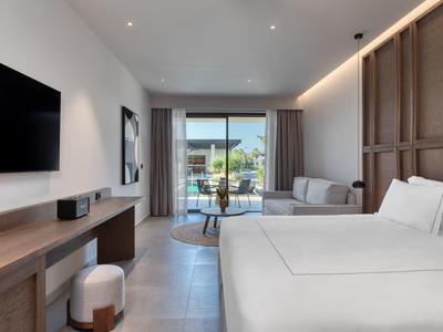 Modern hotel room with large bed, seating area, and balcony access with sea view.
