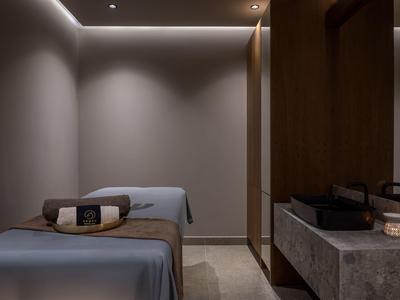 Modern spa room with massage table, soft lighting, and stone sink.