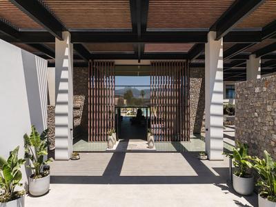 Modern hotel entrance with wooden lattice gate, sun shadows, and potted plants.