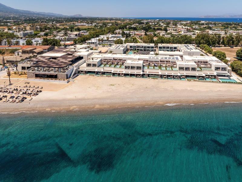 Wide sandy beach with sun loungers in front of a large hotel complex by the sea.