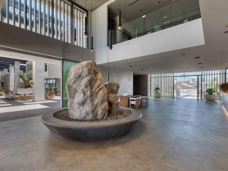 Modern hotel lobby with large stone sculpture in the center and large glass windows.