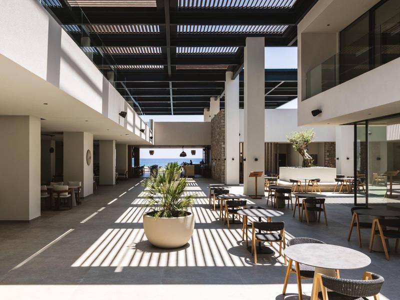 Modern hotel outdoor area with tables, chairs, and a view of the sea.