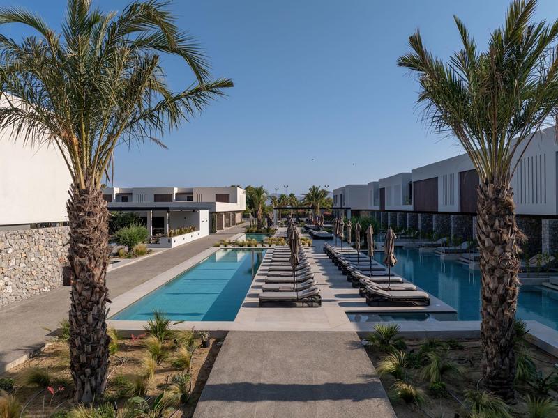 Modern hotel pool with lounge chairs and palm trees under clear sky.