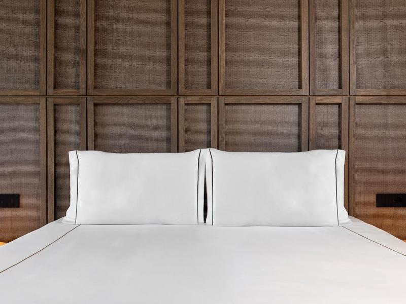 Modern hotel bed with white bedding against a wooden paneled wall