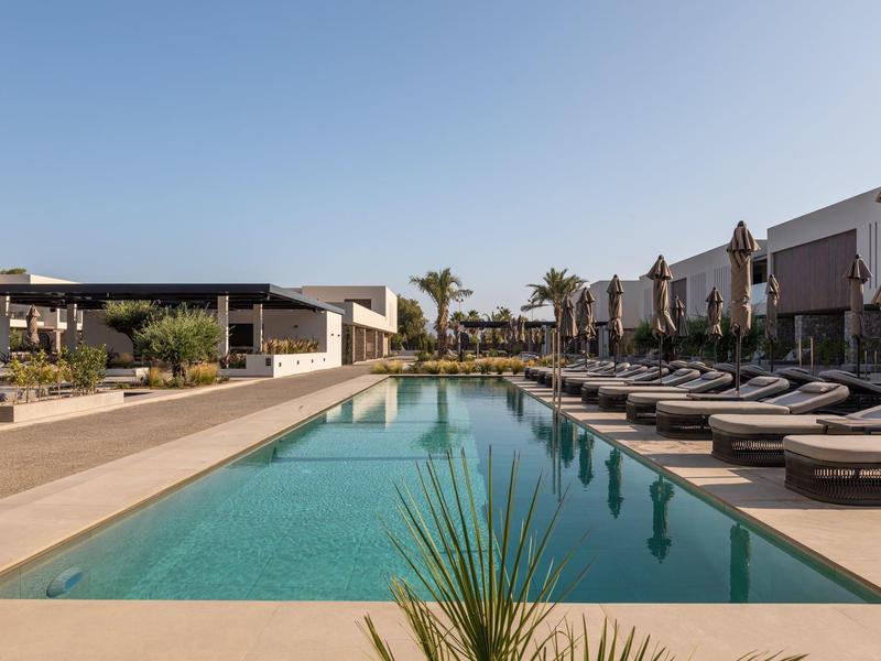 Modern outdoor pool area with sun loungers and umbrellas next to a hotel.