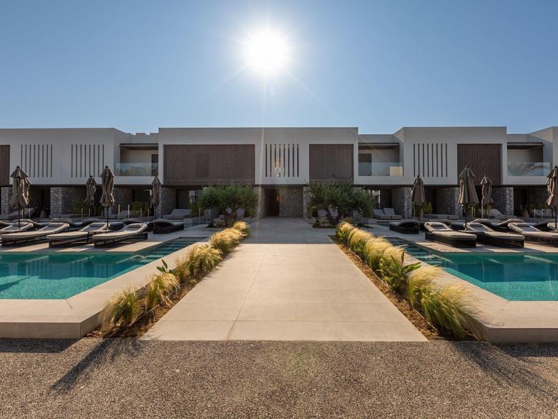 Symmetrical view of a pool area with sun loungers and modern buildings under a sunny sky.