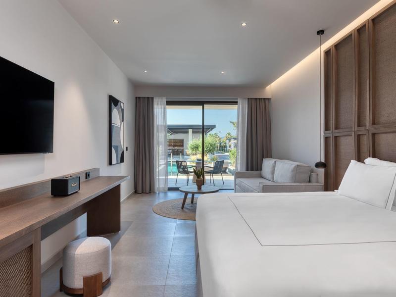 Modern hotel room with large bed, seating area, and balcony access with sea view.