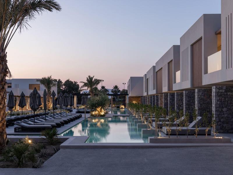 Modern hotel pool in evening light with sun loungers and palm trees by contemporary buildings.