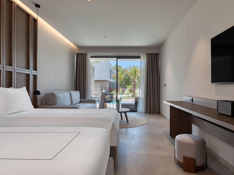 Bright hotel room with two beds, sofa, and balcony access.