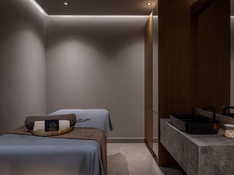 Modern spa room with massage table, soft lighting, and stone sink.