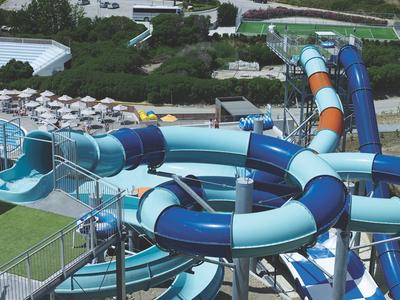 Duże niebieskie zjeżdżalnie wodne wiją się przez park wodny z wieloma parasolami.