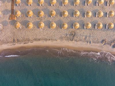 Zdjęcie z lotu ptaka plaży z równomiernie rozmieszczonymi parasolami i spokojnym morzem.