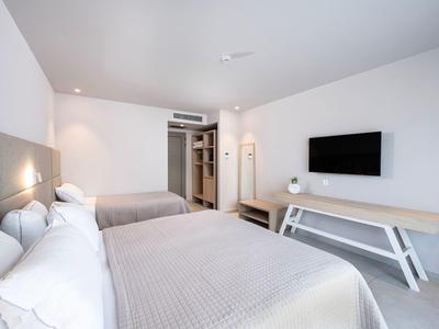 Nowoczesny pokój hotelowy z dwoma łóżkami, telewizorem i minimalistycznym wystrojem.