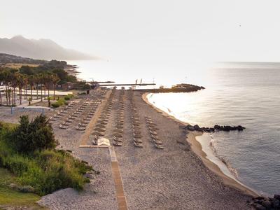 Pusta piaszczysta plaża z parasolami przy spokojnym morzu i kilkoma budynkami w tle.