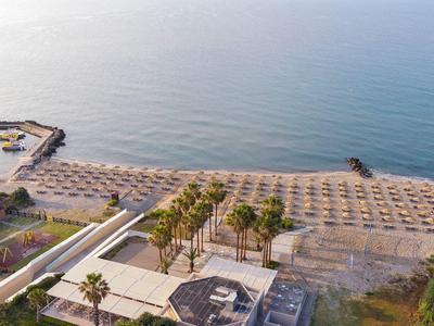 Widok z lotu ptaka na cichą plażę z rzędami parasoli i pomostem wychodzącym na morze.