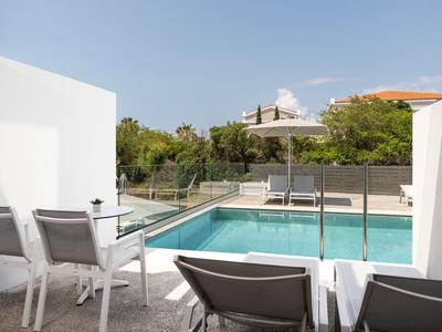 Nowoczesny basen z leżakami i parasolem za szklaną balustradą w słoneczny dzień.