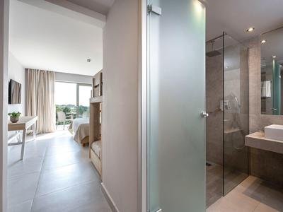 Korytarz z łóżkami piętrowymi po lewej i łazienką z prysznicem po prawej w nowoczesnym pokoju hotelowym.