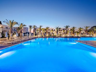 Großer beleuchteter Pool mit Palmen und Hotelgebäuden bei klarem Himmel in der Nacht