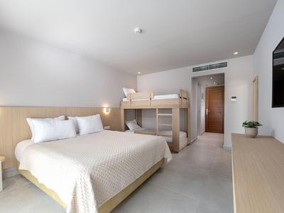 Nowoczesny pokój hotelowy z łóżkiem podwójnym, łóżkiem piętrowym, telewizorem i prostym wystrojem.