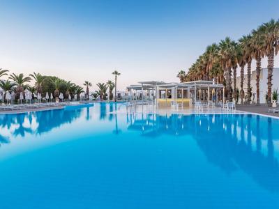 Großer Pool mit klarem Wasser, umgeben von Palmen und einer Poolbar im Hintergrund.