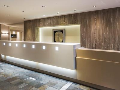 Nowoczesna recepcja hotelowa z podświetlanym kontuarem i drewnianą ścianą.