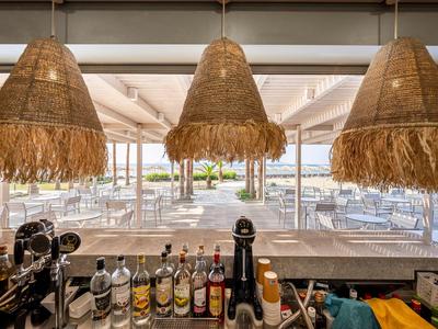 Barbereich mit Korbhängelampen und Blick auf eine Terrasse am Wasser.