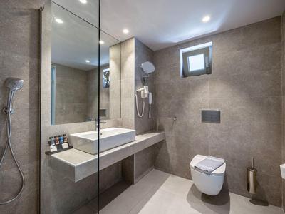 Nowoczesna łazienka hotelowa z prysznicem bez brodzika, umywalką i toaletą w neutralnych kolorach.