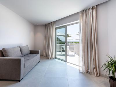 Minimalistyczny salon z szarą sofą, dużymi oknami i jasnymi zasłonami.