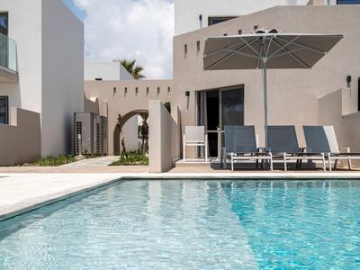 Nowoczesny basen z leżakami i parasolem przed białym budynkiem.