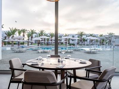 Okrągły stół z czterema krzesłami na balkonie z widokiem na basen i palmy w ośrodku.