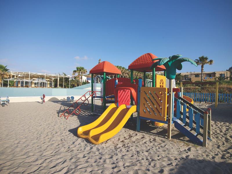 Kolorowy plac zabaw z zjeżdżalniami na piaszczystym podłożu pod czystym niebem w ośrodku wypoczynkowym.