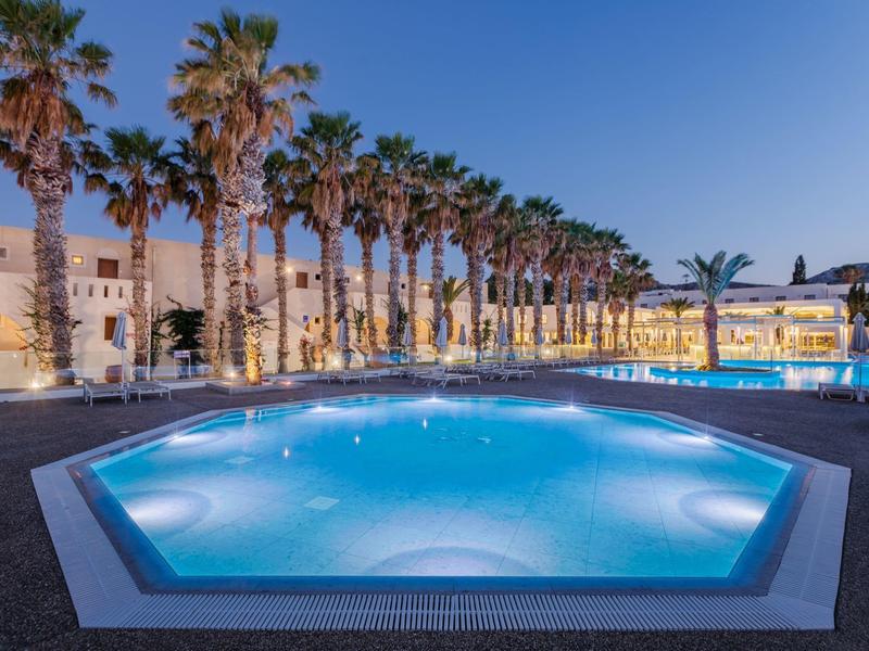 Oświetlony basen z rzędem palm i hotelami o zmierzchu