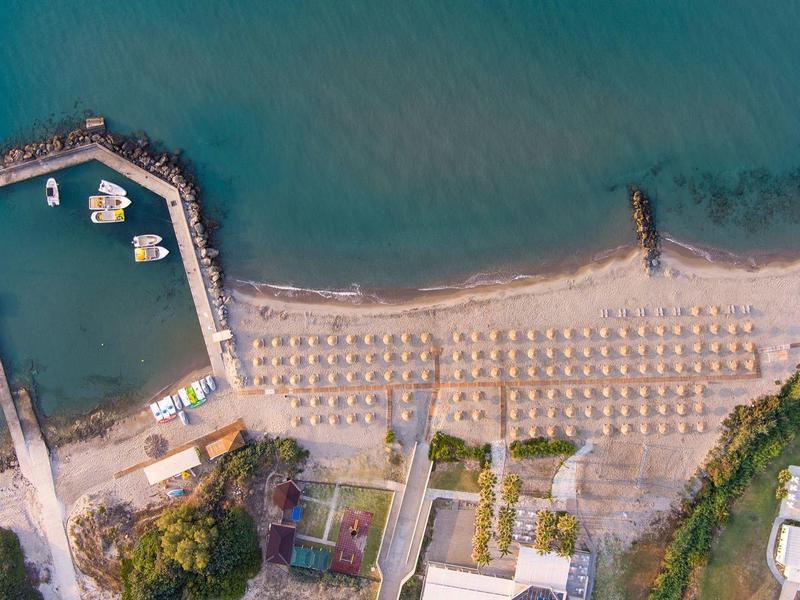 Zdjęcie z lotu ptaka plaży z rzędami parasoli, pomostami i czystą wodą.