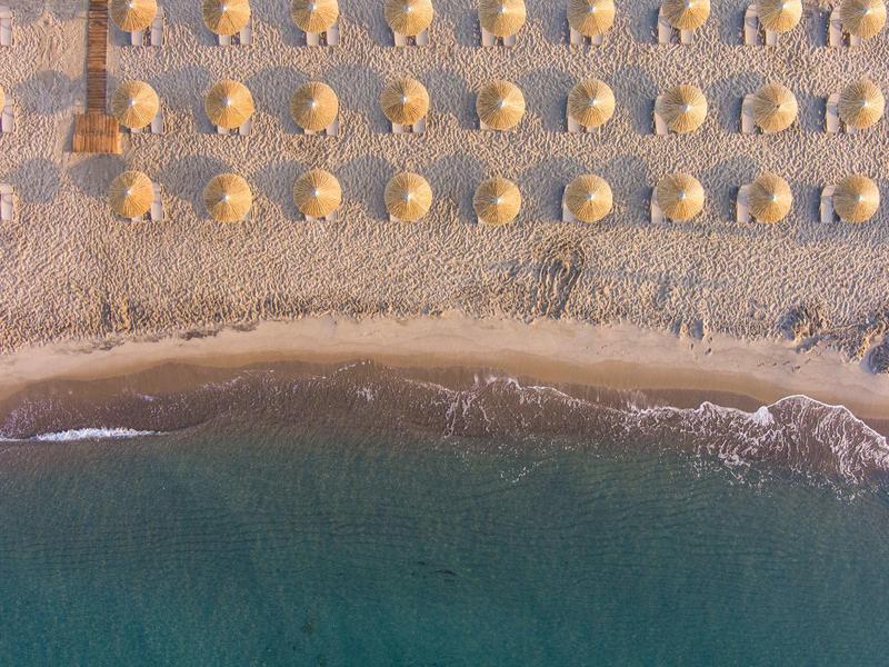 Zdjęcie z lotu ptaka plaży z równomiernie rozmieszczonymi parasolami i spokojnym morzem.