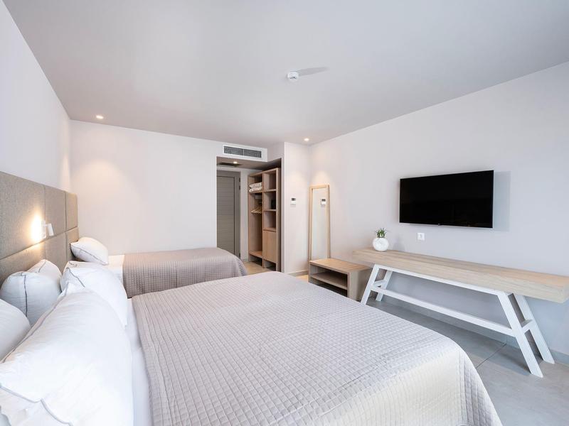 Nowoczesny pokój hotelowy z dwoma łóżkami, telewizorem i minimalistycznym wystrojem.