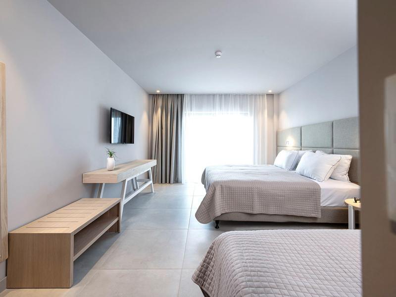 Jasny pokój hotelowy z dwoma łóżkami, telewizorem i biurkiem przed oknem z zasłonami.