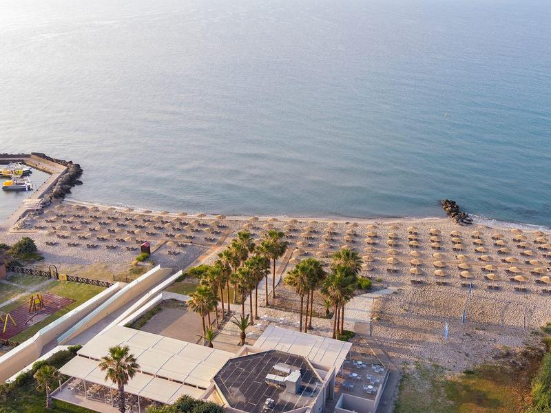 Widok z lotu ptaka na cichą plażę z rzędami parasoli i pomostem wychodzącym na morze.