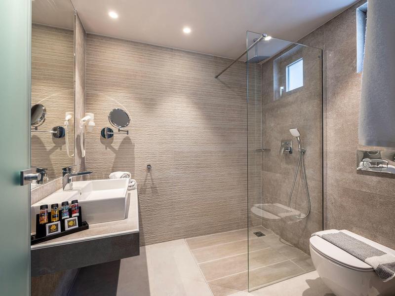 Nowoczesna łazienka hotelowa z prysznicem bez brodzika, toaletą i umywalką.