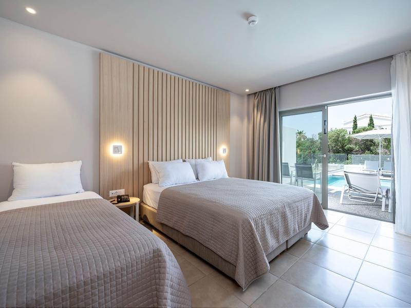 Nowoczesny pokój hotelowy z dwoma łóżkami, stołem i dostępem do tarasu z widokiem na basen.