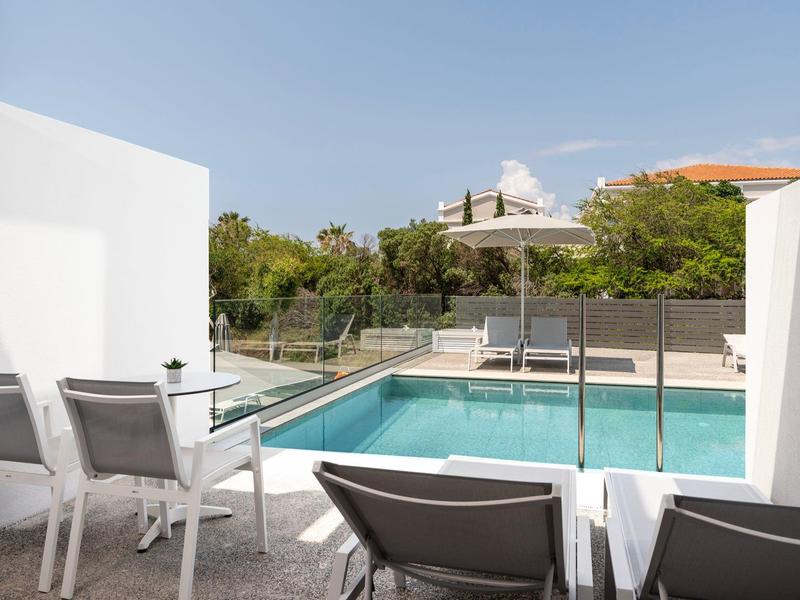 Nowoczesny basen z leżakami i parasolem za szklaną balustradą w słoneczny dzień.