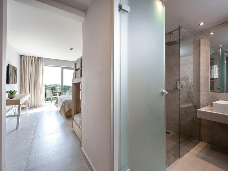 Korytarz z łóżkami piętrowymi po lewej i łazienką z prysznicem po prawej w nowoczesnym pokoju hotelowym.