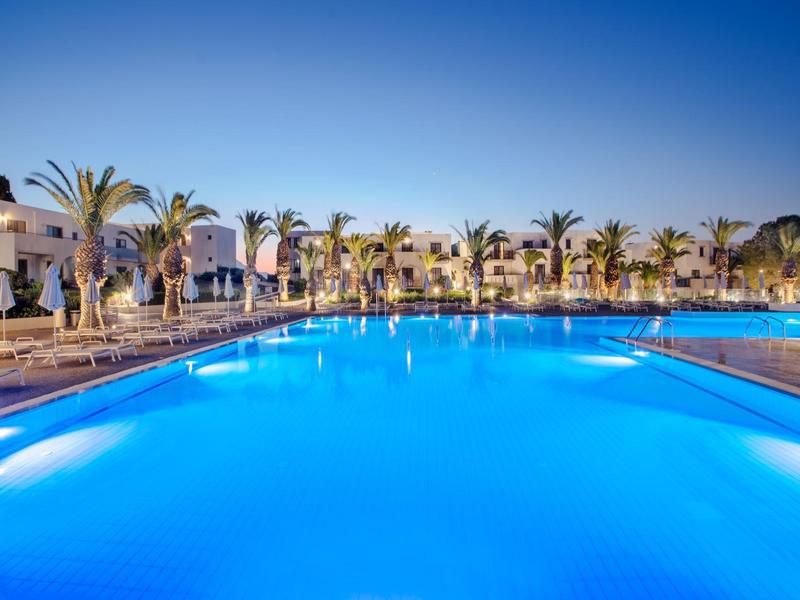 Oświetlony duży basen przed hotelem z palmami pod czystym niebem.