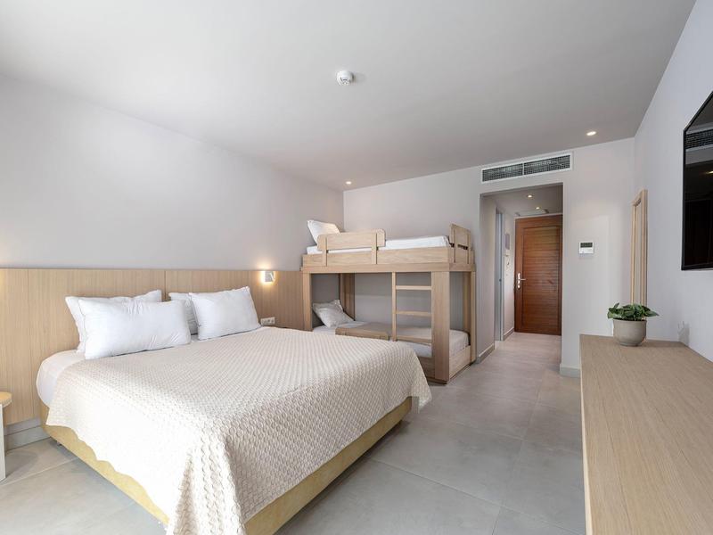 Nowoczesny pokój hotelowy z łóżkiem podwójnym, łóżkiem piętrowym, telewizorem i prostym wystrojem.