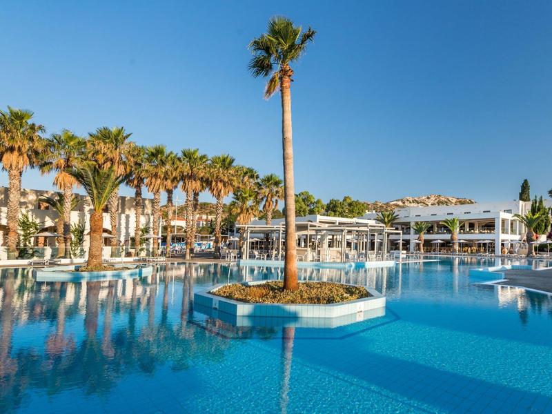 Duży basen hotelowy z palmami i niebieską wodą pod czystym niebem.