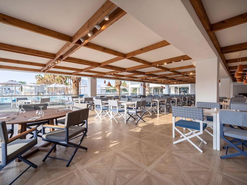 Jasny taras hotelowy z drewnianym sufitem, stołami i krzesłami z widokiem na zewnątrz.